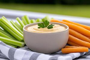 Hummus with carrot and celery sticks garnished with parsley on a checkered napkin photo
