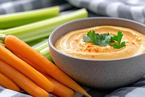 Bowl of hummus seasoned with paprika and decorated with parsley with fresh celery and carrot sticks photo