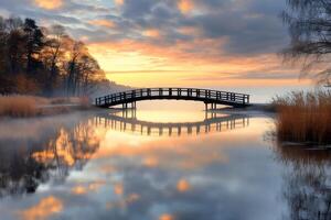 Wooden bridge reflecting on calm lake at sunrise photo