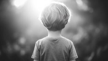 Young child gazing into the distance. A young child stands quietly, with soft light illuminating their hair, lost in thought and exploration. photo