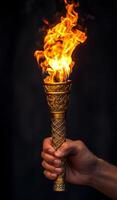 Flame bursts from a tall torch. A hand grips an intricately designed torch emitting vibrant flames, symbolizing light and celebration in darkness. photo
