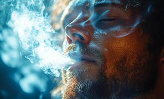 Man exhaling smoke in a dimly lit space. A man with a beard exhales smoke while lost in thought in a softly lit environment. photo