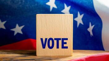 Vote block with flag behind. A wooden block displaying the word vote stands prominently in front of a textured flag featuring stars and stripes. photo