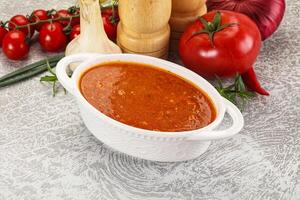 A bowl of tomato sauce next to a knife and a tomato photo