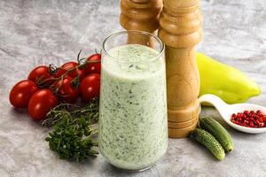A glass of green smoothie next to a pepper and a tomato photo