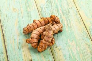 A pile of raw tumeric root on a wooden table photo