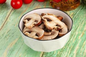 A bowl of mushrooms on a table with a bottle of wine photo