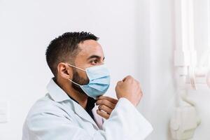 Portrait in sideview of a dentist hispanic male holding a facemask photo