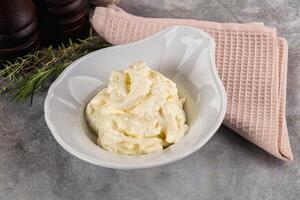 A bowl of cream sits on a table next to a towel photo