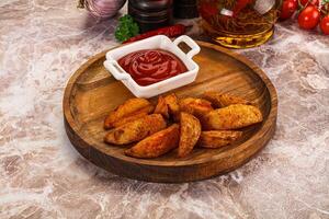 A wooden plate with some potatoes and ketchup photo