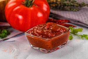 A tomato and a bowl of sauce next to a cutting board photo
