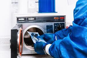 unrecognizable person in bio security suit holding tools and putting them into a machine to sterilize them. photo