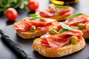 Delicious bruschetta with coppa, olives and herbs resting on slate serving tray photo