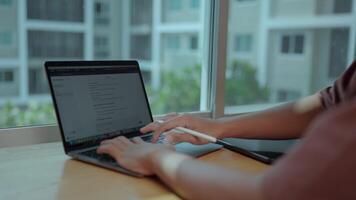 Working from Home. Hands typing on laptop keyboard, tablet nearby, city view outside window. Focus on productivity and remote work. Displays a web page with a text interface using a modern chat tool. video