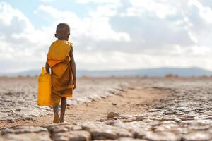 A young African boy in traditional attire walks alone, holding a yellow container against a dramatic sky. photo