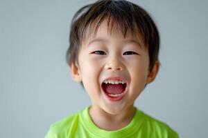 A joyful Asian boy, around 5 years old, smiles widely with a bright, cheerful expression against a soft gray background. photo