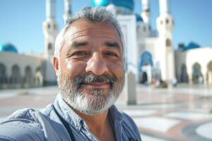 A middle-aged Middle-Eastern man smiling in front of a stunning mosque, showcasing a vibrant blue sky. photo
