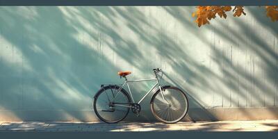 A sleek silver bicycle with an orange seat leans against a turquoise wall, casting striking shadows under autumn sunlight. photo