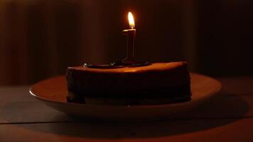 The flame on the candle flutters in the wind and goes out. Make a wish. Birthday cake in a plate with the number 1. Flickering fire on a dark background. video