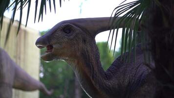 A giant parasaurolophus shakes its head, displayed in a park on a sunny summer day. Dinosaur on the background of the sky and trees video