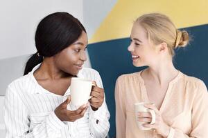 Female call centre operators having coffee and talking during their break at modern open space office, copy space. Positive hotline consultants having friendly chat, enjoying each other's company photo