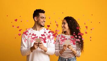 A couple shares a joyful moment together, holding smartphones while surrounded by heart graphics. They are celebrating their love on St. Valentines Day, conveying affection and connection. photo