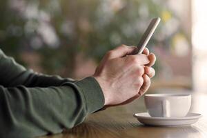Cropped image of man sitting at cafe, drinking tea, using smartphone, side view photo