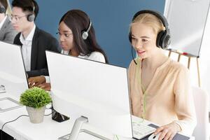 Multiethnic call centre operators with headsets talking to clients online at modern office. Focused hotline consultants working in telecommunications or tech support, indoors photo