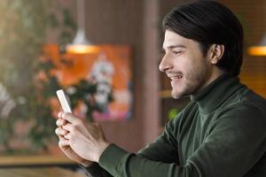 Cheerful entrepreneur using smartphone while drinking coffee at cafe, empty space, side view photo
