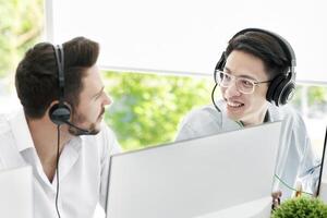 Male customer support service operators with headsets talking at light office. Positive hotline centre colleagues having friendly conversation behind their computer monitors, indoors photo