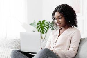 Online Education. Young Black Woman Studying With Laptop At Home, Sitting On Couch And Browsing Internet On Computer, Enjoying Distance Learning, Watching Webinar, Typing On Keyboard, Free Space photo
