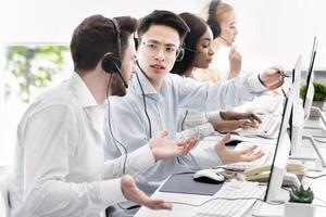User support service concept. Hotline operator helping his coworker at call centre. Customer care agents communicating to each other, solving client's problem at modern office photo