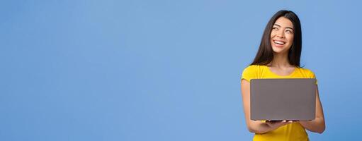 Online Offer. Smiling Pensive Asian Woman Holding Laptop And Looking Away At Copy Space Over Purple Background, Enjoying Remote Work Or Distance Learning, Panorama With Copy Space photo