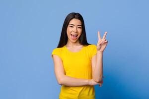 Cheerful Asian Girl Gesturing Peace While Posing Over Purple Studio Background, Copy Space photo