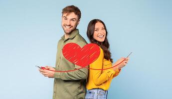 A joyful couple stands back to back, each holding a smartphone. They celebrate St. Valentines Day by exchanging affectionate messages. Their smiles express love and connection in a playful way. photo