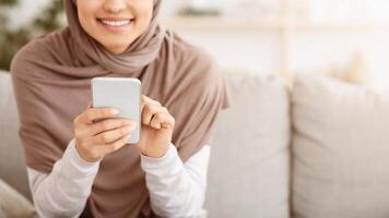 Modern Communication. Closeup Of Unrecognizable Muslim Woman In Hijab Using Smartphone At Home, Browsing Internet Or Texting With Friends, Panorama photo