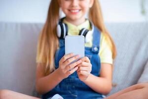 Enjoying Free Time. Unrecognizable girl using her cell phone sitting on sofa, selective focus on gadget photo