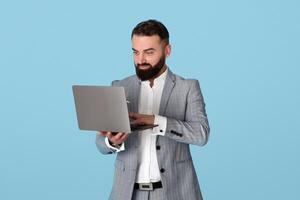 Online business concept. Confident young entrepreneur using laptop computer for remote work or communication, watching educational webinar, having meeting on blue studio background photo