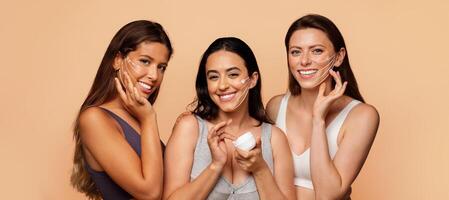 Three multiethnic women are engaging in a relaxing skin care session, applying rejuvenating masks while smiling and pampering themselves in a warm, inviting setting. photo