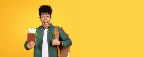 Enthusiastic young African American guy traveler holds a passport and gives a thumbs up, symbolizing approval for travel adventures on a yellow backdrop photo