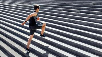 Cardio workout. Slim guy in sportswear doing exercises and runs up the stairs, raising his legs high in sunlight, free space photo