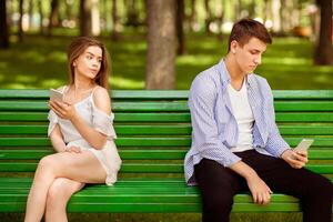 Relationship problem. Bored millennial couple using phones on dull date at park photo