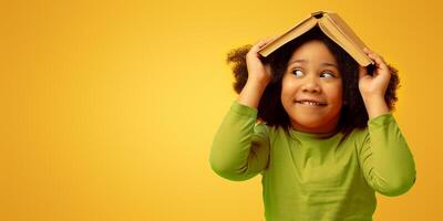 Early Education And Development. Funny Little Black Girl Hiding Under Opened Book, Isolated On Yellow Background, Panorama With Copy Space photo