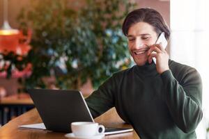 Successful entrepreneur having conversation on smartphone while working with laptop at cafe, copy space photo