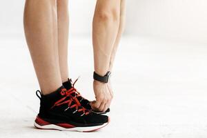 Covid-19 quarantine, workout at home alone and health care. Woman athletic trainer in sneakers and fitness tracker doing warm up in interior of gym or at home with equipment, cropped, free space photo