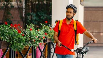 City food, delivery and bike. Courier with beard, protective helmet and yellow bag, walking the street with bicycle and looking for client address photo