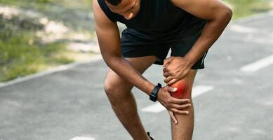 African American jogger suffering from pain in his knee during morning run at park photo