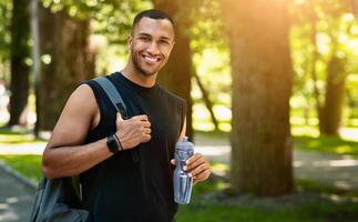 Portrait of smiling black sportsman with backpack and bottle of water after his training at park, panorama photo