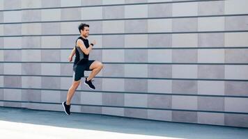 Jogging with jumping. Guy runs at path near gray brick wall in city in daylight, free space photo