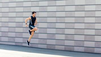 Freeze in air at training. Slender guy jumping and running on street on gray wall background, free space photo